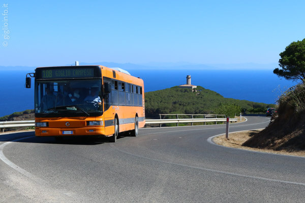 Autobus sulla strada dell'Isola del Giglio con vista antico faro e mare