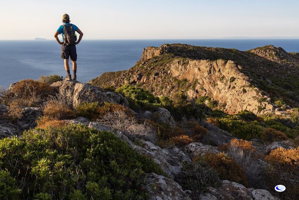 Persona che fa trekking e ammira la vista sull'arcipelago toscano dalla vetta Isola di Capraia