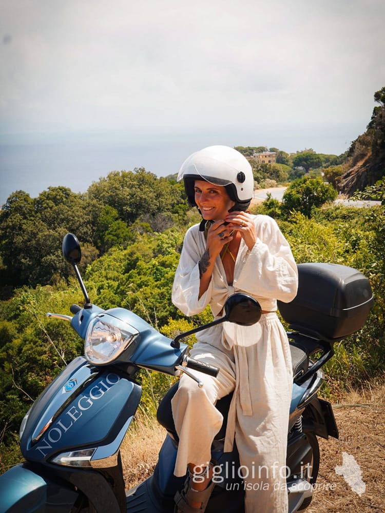 Ragazza sullo scooter che si allaccia il casco - Giglionoleggio Noleggio Scooter Isola del Giglio Porto